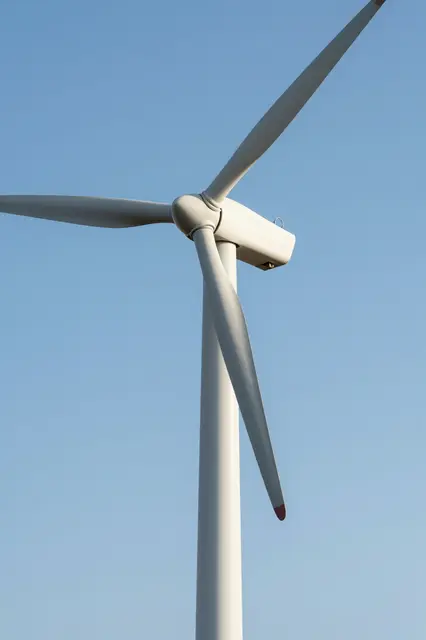 Low angle view of a white wind turbine with red blade tips against a clear cloudless blue sky
