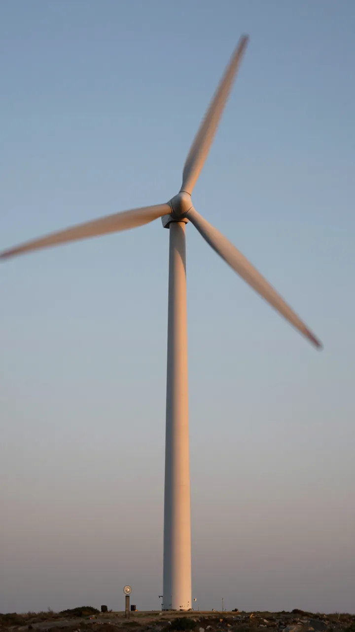Wind turbine with motion-blurred rotating blades stands against a fading dusk sky