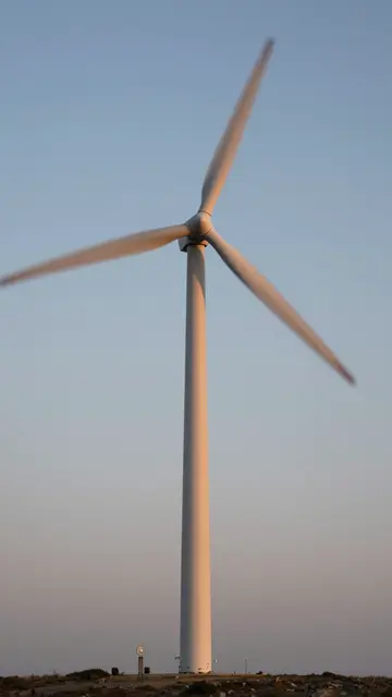 Wind turbine with motion-blurred rotating blades stands against a fading dusk sky