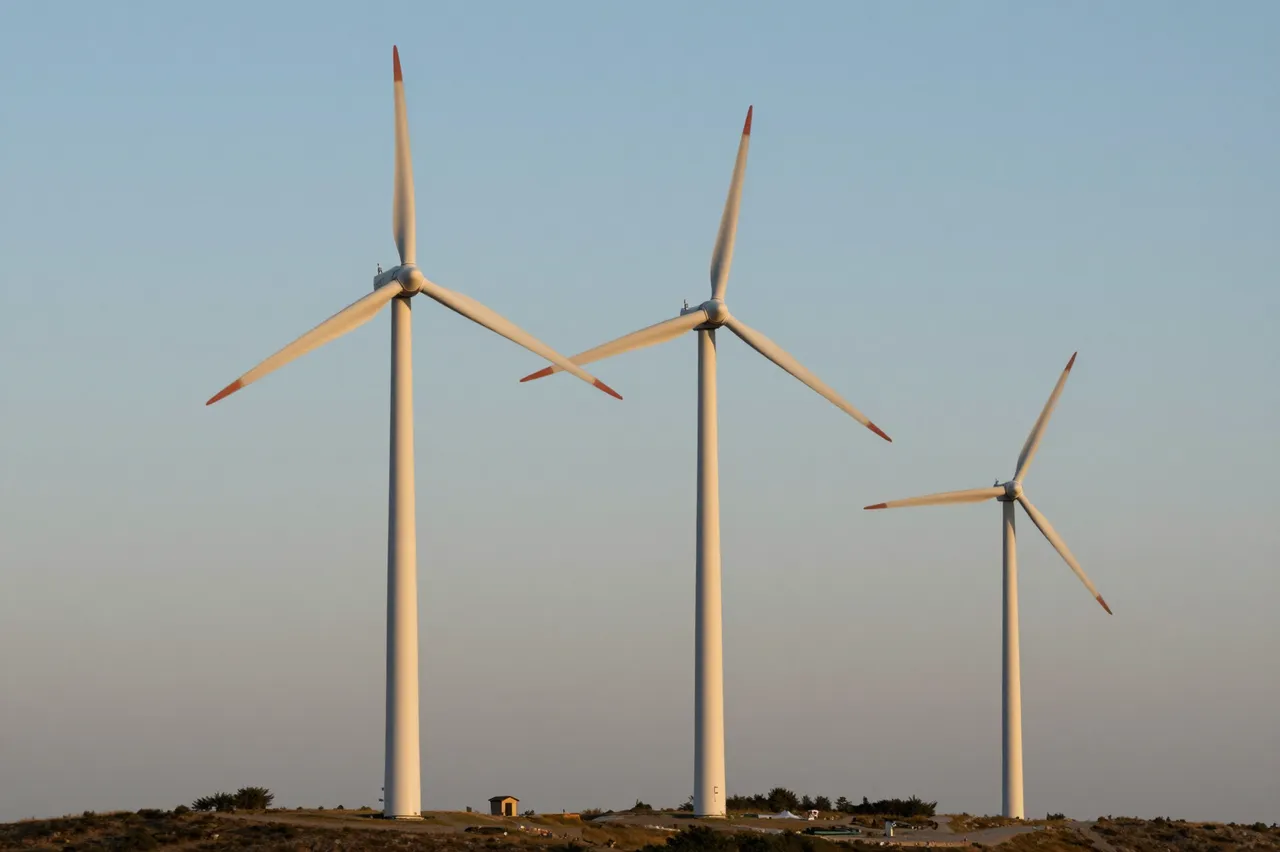 Three wind turbines stand on a grassy hill beneath a soft gradient dawn sky