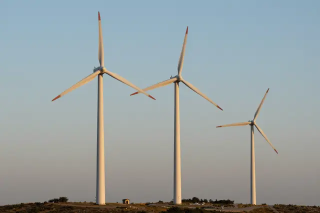 Three wind turbines stand on a grassy hill beneath a soft gradient dawn sky