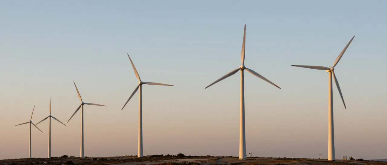A row of wind turbines stands along a ridgeline beneath a soft gradient sunset sky