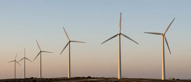 A row of wind turbines stands along a ridgeline beneath a soft gradient sunset sky