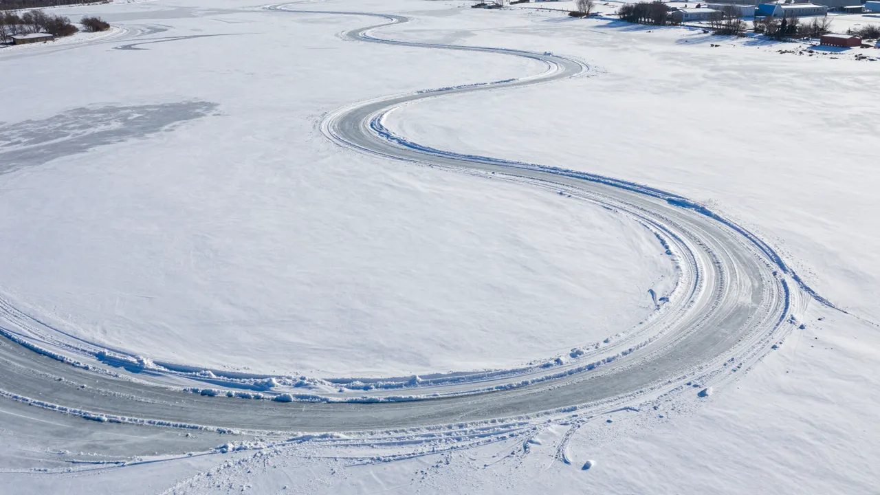 Aerial perspective of a winding cleared ice track snaking across a vast snow-covered winter plain
