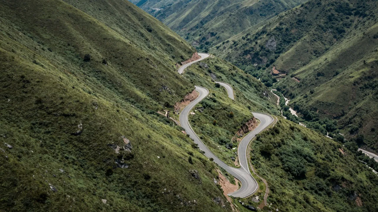 Aerial view of a serpentine paved road with tight hairpin bends snaking across lush green mountain slopes