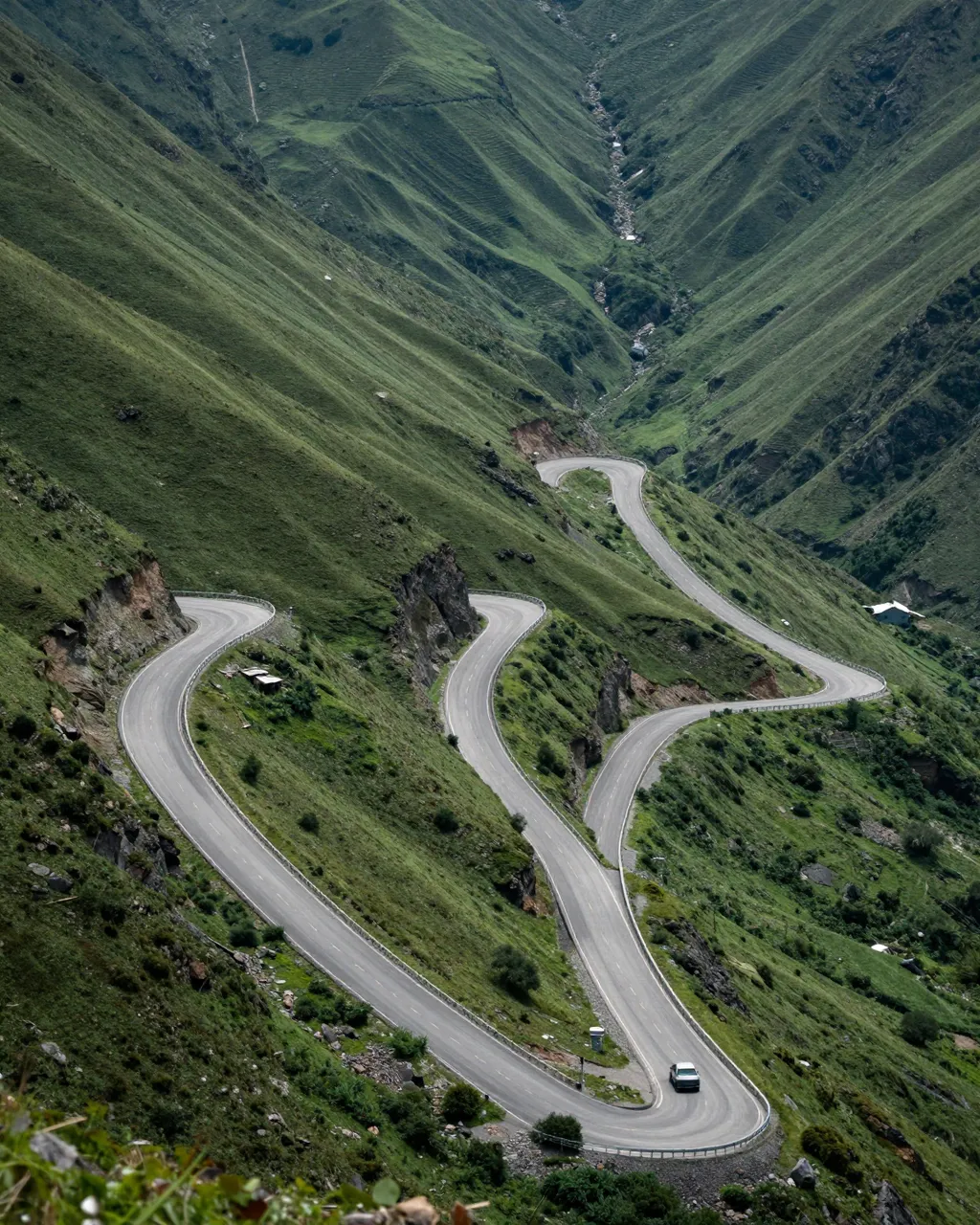 High angle view of a zigzag paved road descending a steep grassy mountain valley