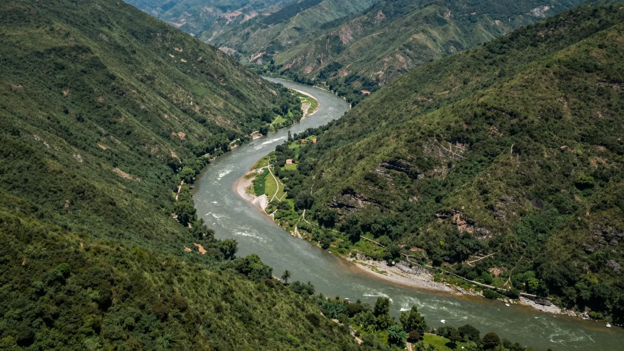 Aerial view of a winding wide river cutting through lush green mountain valley slopes