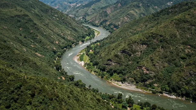 Aerial view of a winding wide river cutting through lush green mountain valley slopes