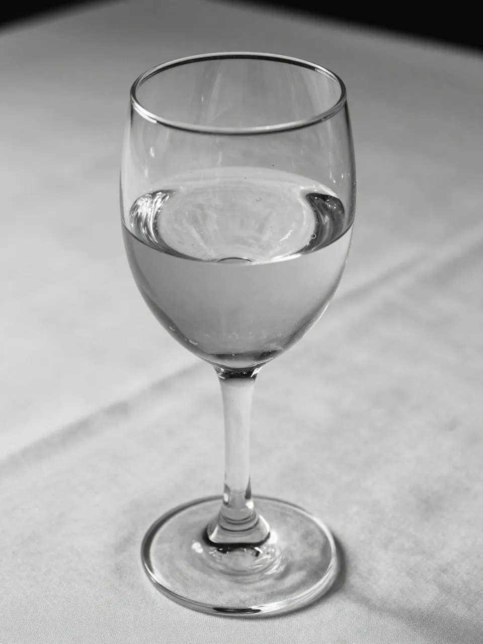 Black and white close-up of a half-full crystal wine glass resting on a light tablecloth