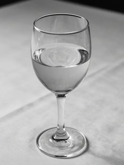 Black and white close-up of a half-full crystal wine glass resting on a light tablecloth