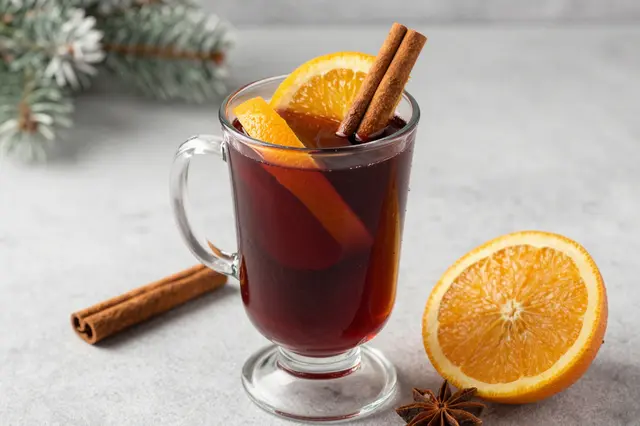 Glass mug of spiced mulled wine garnished with orange slices and cinnamon on a light gray winter tabletop