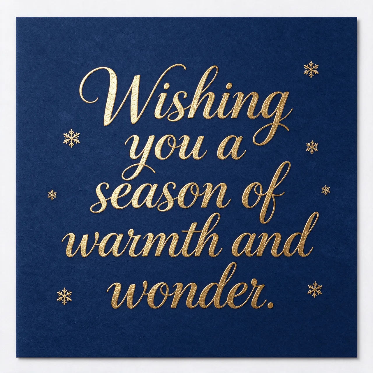 Gold foil script reading "Wishing you a season of warmth and wonder." with small gold snowflakes on a deep navy card