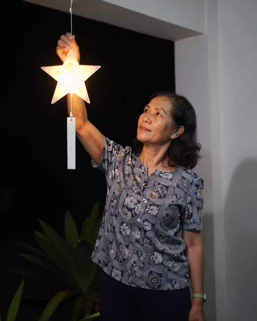 Middle aged Southeast Asian woman adjusts a glowing capiz star lantern on a porch at night