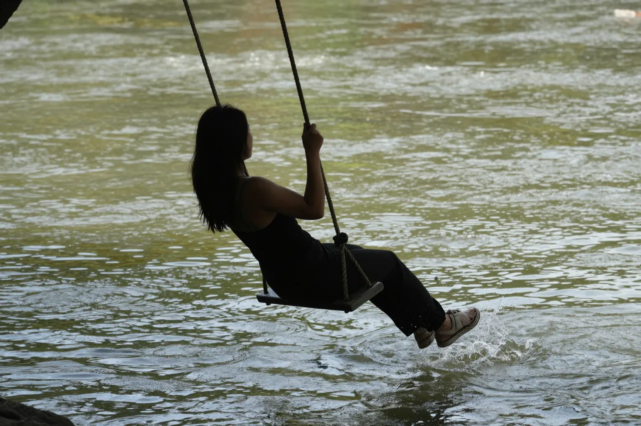 Silhouette of a woman sitting on a rope swing with her feet skimming rippling river water