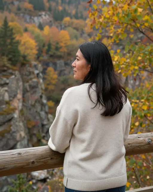Woman in a cream sweater leans on a wooden railing looking out over a rocky autumn gorge