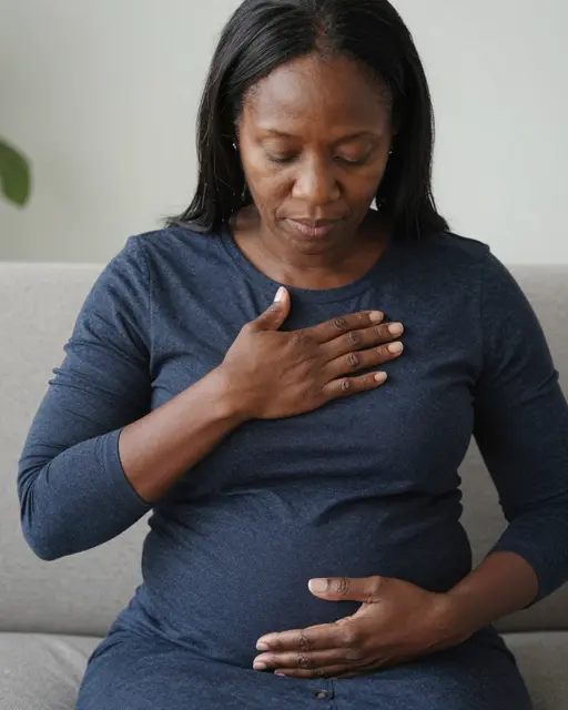 A Black woman in her fifties sits on a sofa with one hand on her chest and one on her belly, eyes closed breathing slowly.