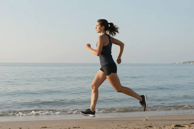 Side view of a woman jogging along a sandy beach shoreline next to calm ocean water at sunrise