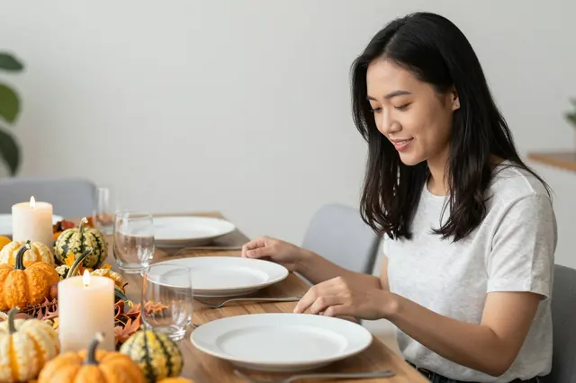 Southeast Asian woman arranging plates on a fall-decorated Thanksgiving dining table