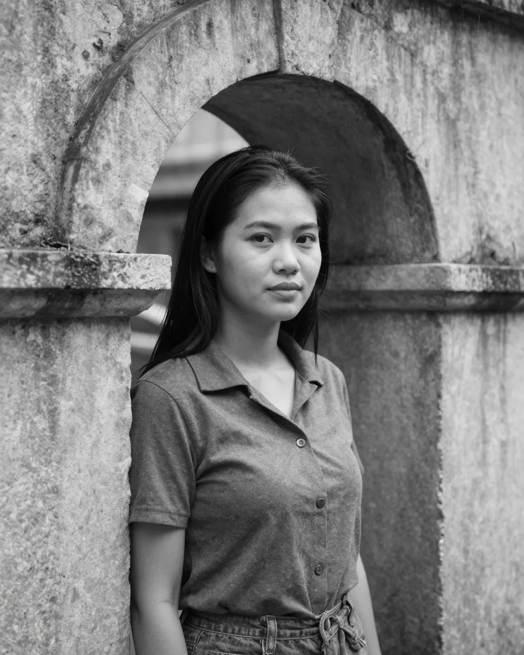 Black and white portrait of a Southeast Asian woman standing under a weathered stone archway