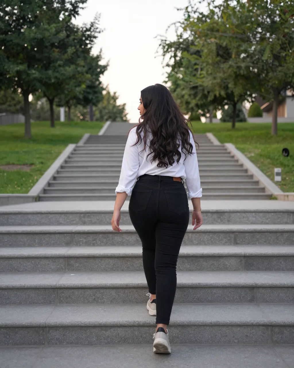 A woman viewed from behind walks up a long concrete park stairway at early dawn