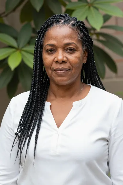 Portrait of a middle-aged Afro-Latina woman with knotless braids wearing a white blouse in a leafy outdoor courtyard