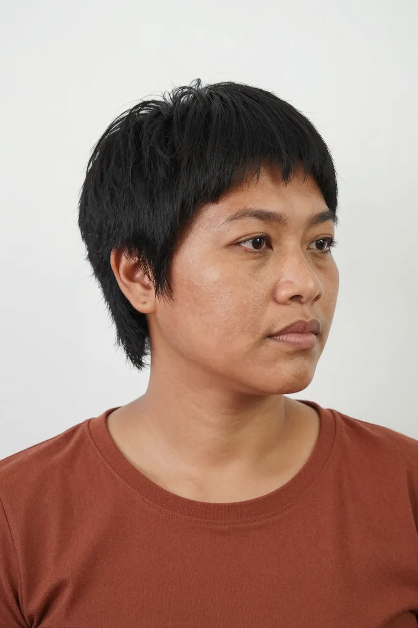 Bust portrait of a thirties Pacific Islander woman with a short modern mullet wearing a rust top against a plain white