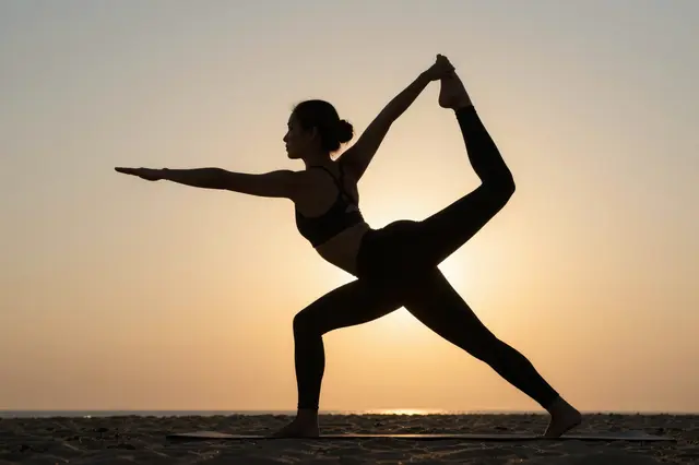 Silhouette of a woman holding a yoga pose on a sandy beach at golden sunset