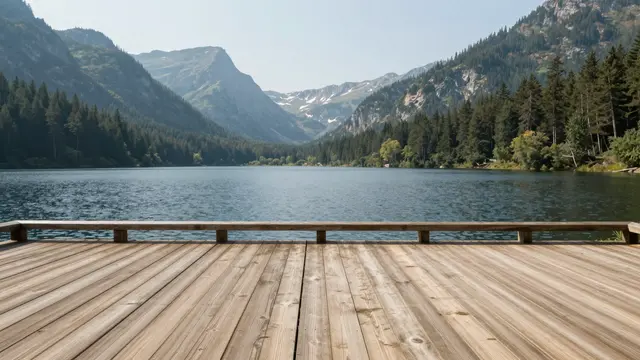 Empty wooden deck with a railing looks out over a calm lake surrounded by forested mountains