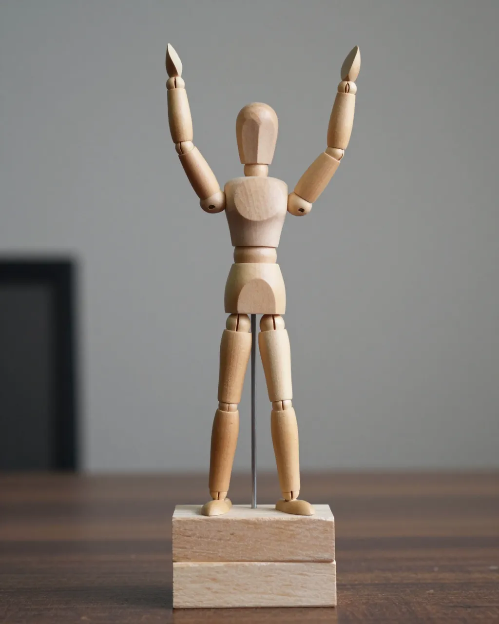 Articulated wooden artist mannequin stands on stacked blocks with arms raised in a victory pose