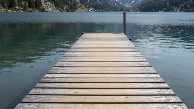 Weathered wooden dock extends out over calm clear lake water toward forested mountain ranges