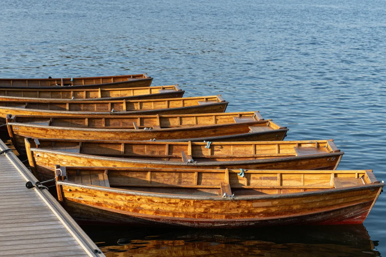 Lined wooden rowboats moored to a wooden dock on calm blue lake water in warm morning light