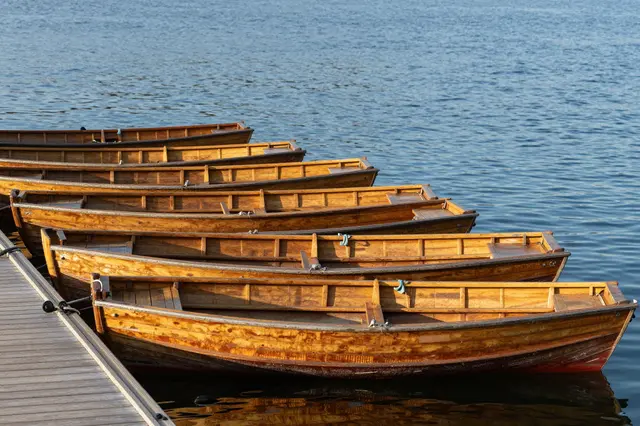 Lined wooden rowboats moored to a wooden dock on calm blue lake water in warm morning light