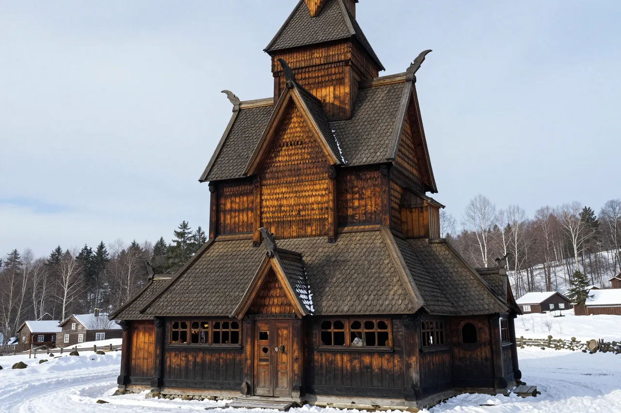 An ornate historic wooden stave church stands in a snow-covered winter landscape under pale overcast skies