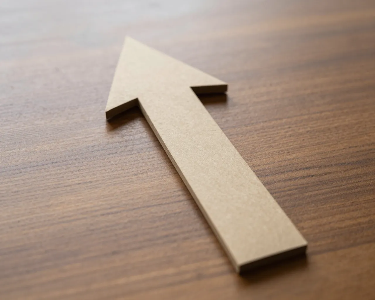 A plain light wood upward-pointing arrow rests diagonally on a dark grained wooden table