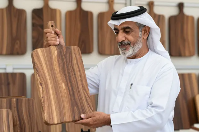 Senior Middle Eastern woodworker holds a walnut cutting board at his craft stall.