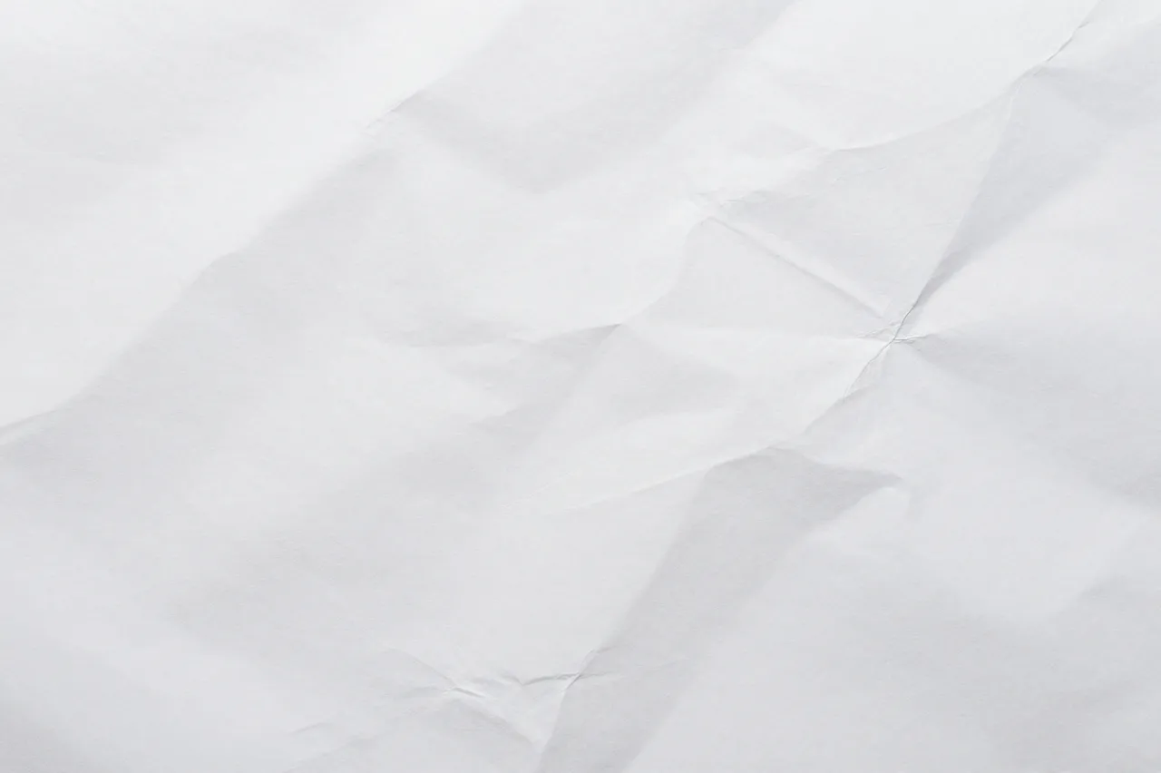 Top view of lightly creased flat white paper filling the full frame with soft diagonal wrinkles