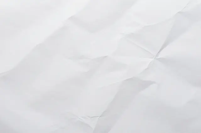 Top view of lightly creased flat white paper filling the full frame with soft diagonal wrinkles