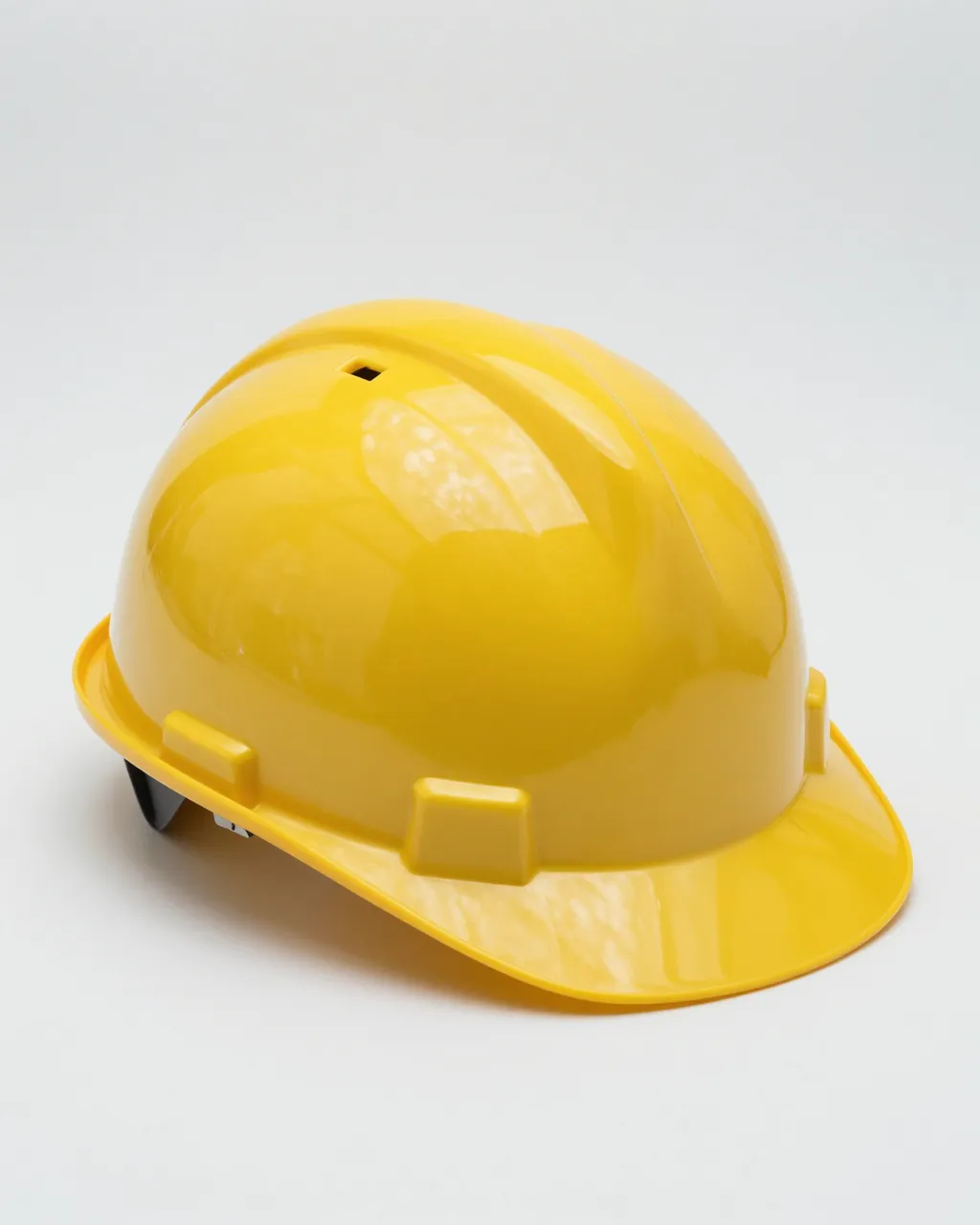 Side view of a glossy yellow hard hat resting on a plain light gray studio background