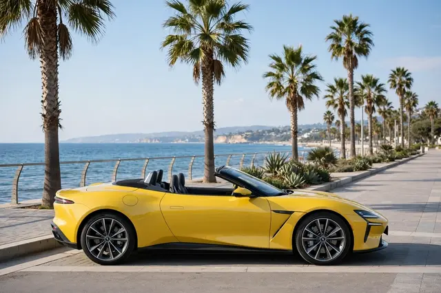 Side view of a bright yellow modern convertible with the top down parked along a palm tree lined seaside promenade