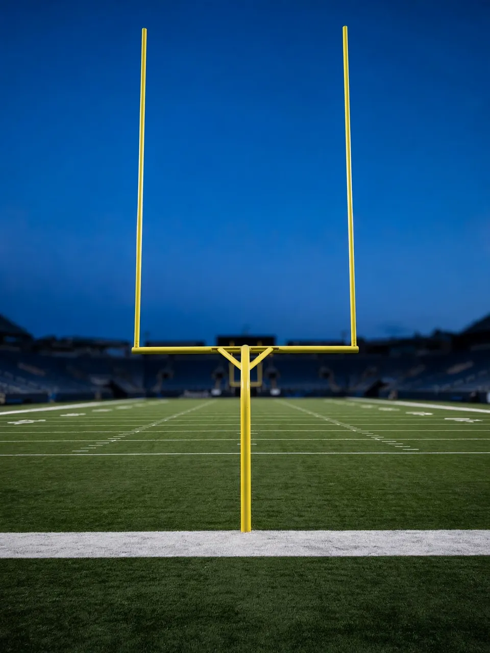 Yellow American football goalpost stands in an empty stadium end zone under a deep blue evening sky