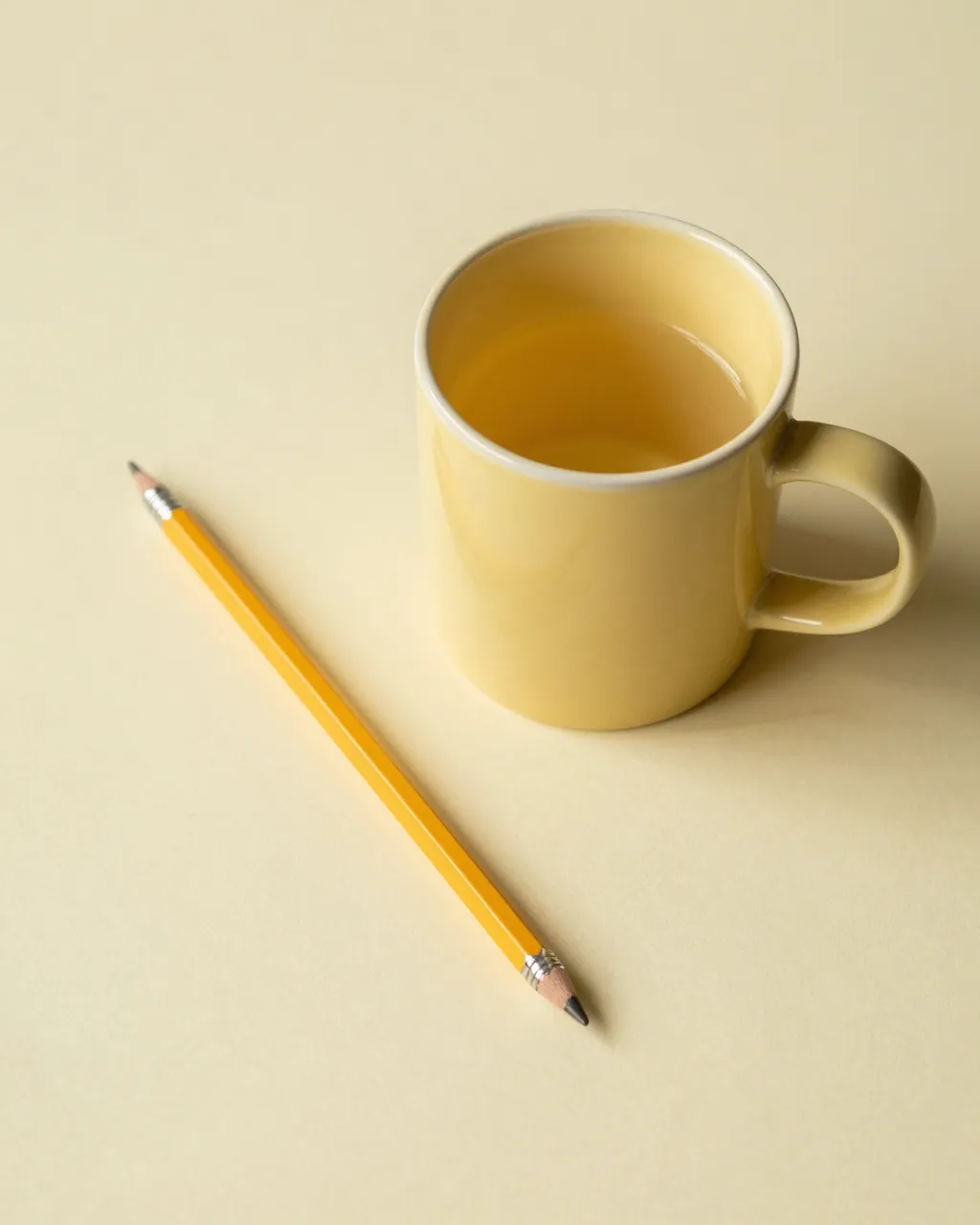 Top view of a butter yellow ceramic mug beside a yellow pencil on a pale yellow surface with empty copy space.