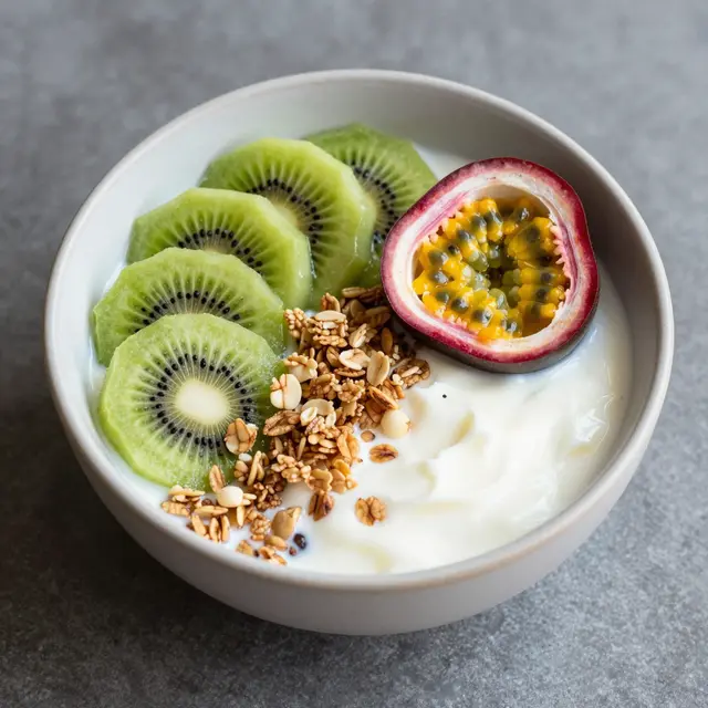 Top view of a yogurt bowl topped with kiwi slices, passion fruit, and granola on a gray countertop.