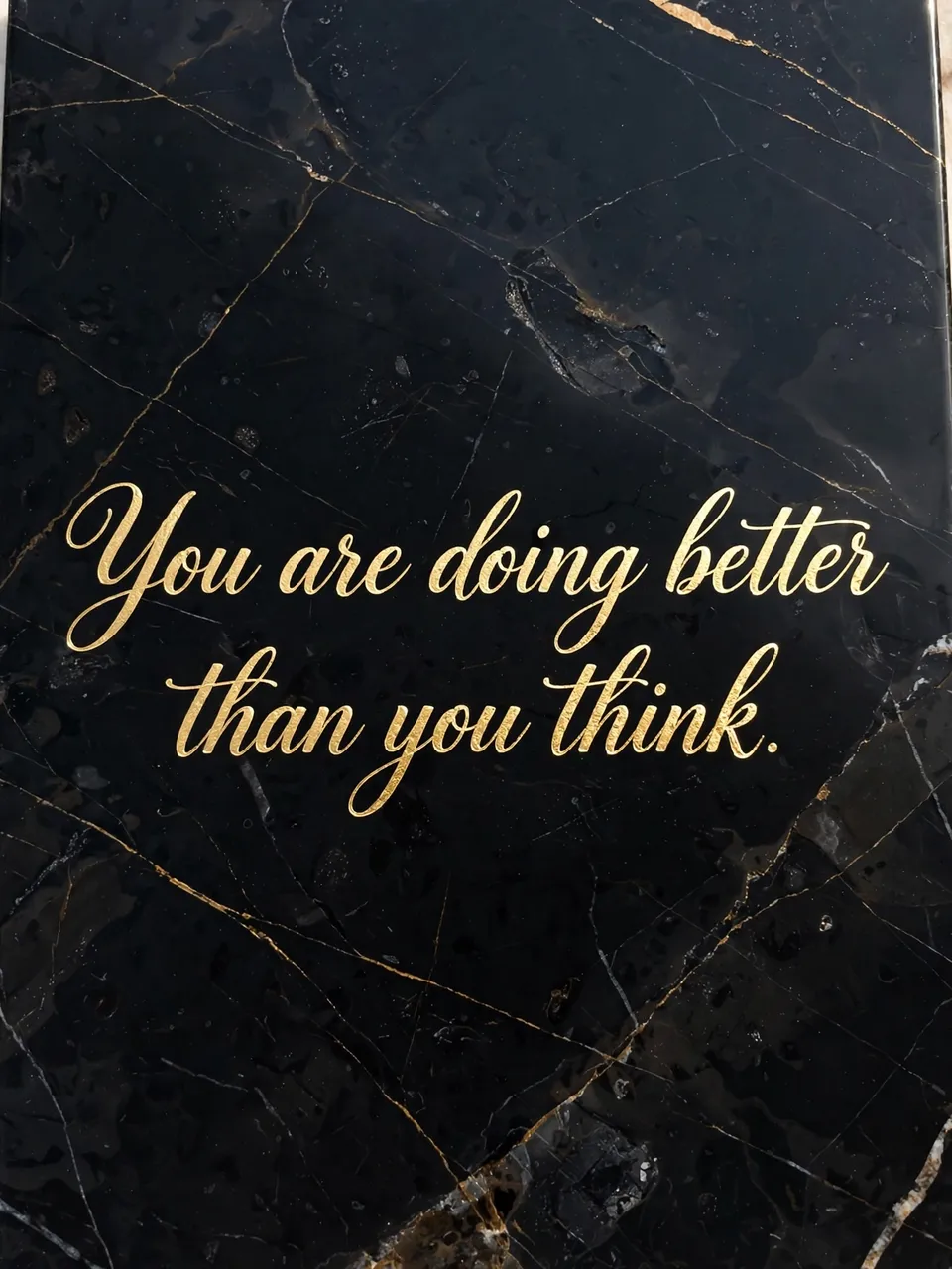 Gold foil script reading "You are doing better than you think." set against polished black veined marble