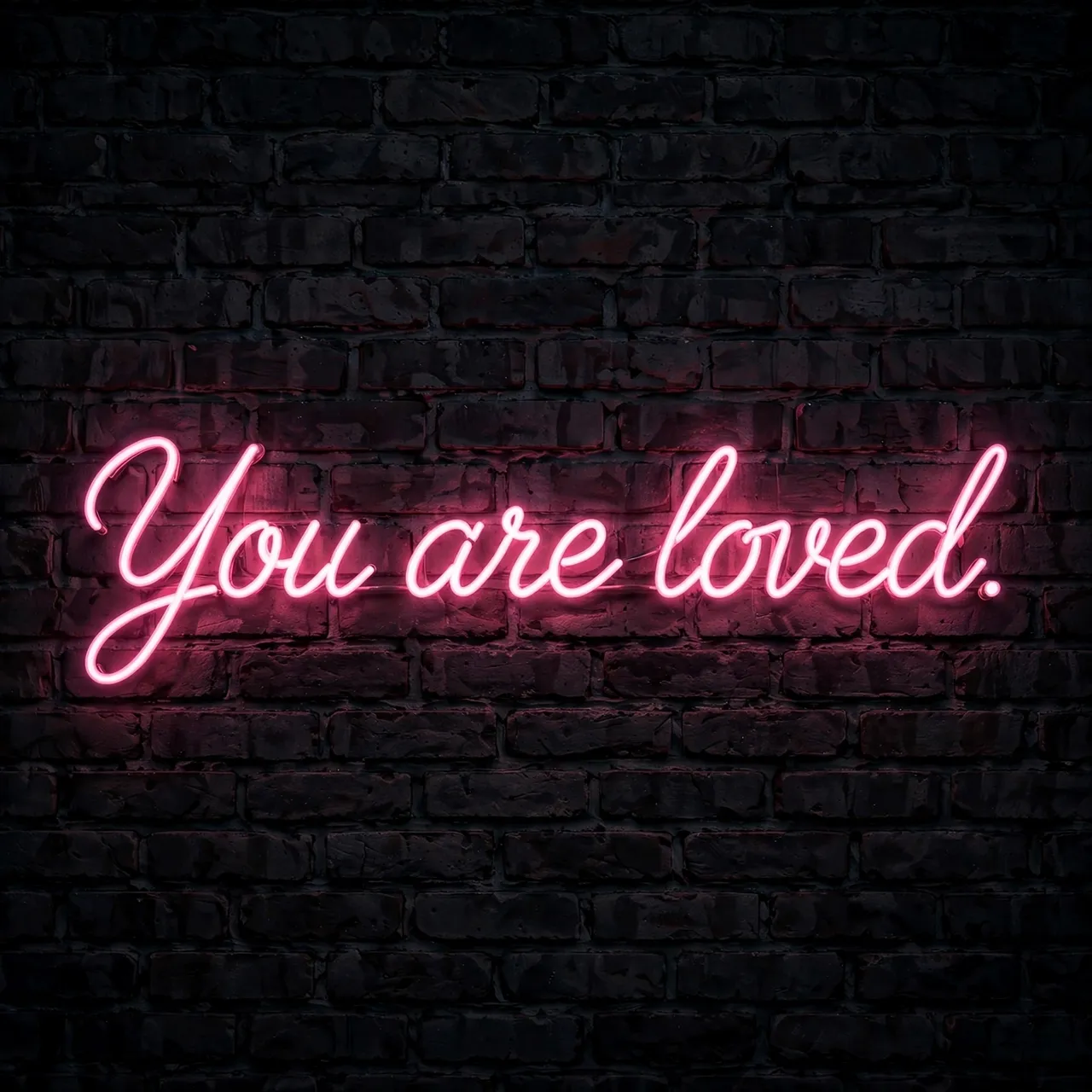 Pink neon sign reading "You are loved." glows against a dark brick wall at night