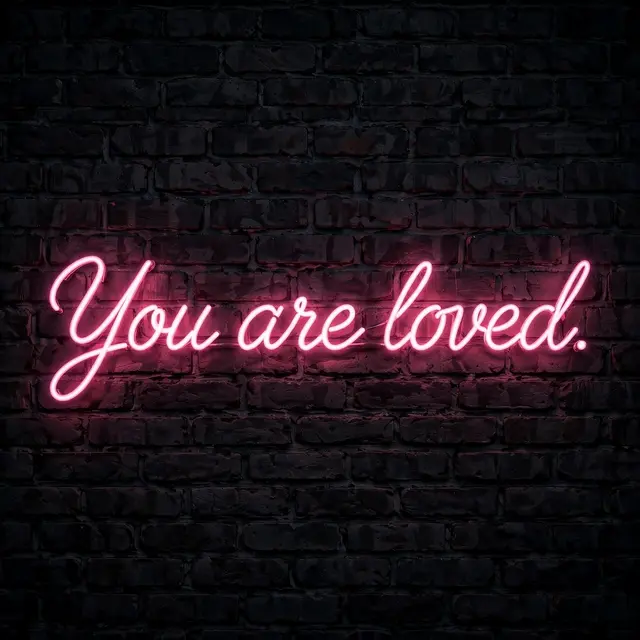 Pink neon sign reading "You are loved." glows against a dark brick wall at night