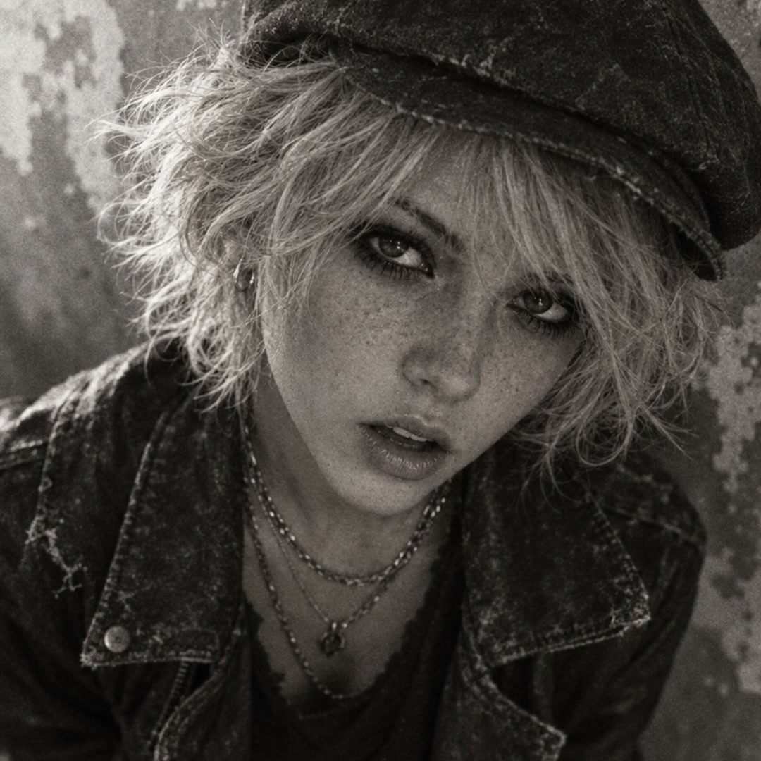 Monochrome close up portrait of a freckled blonde woman in a cap and distressed jacket