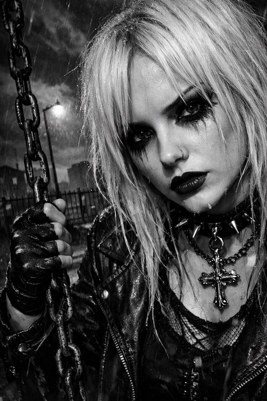 Gothic woman in black-and-white with chains, leather jacket, and cross necklace.