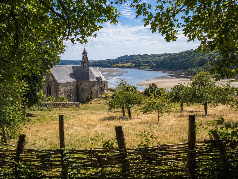 [Framed view of a historic stone chapel overlooking a winding tidal estuary, rural Brittany France on a sunny summer day]
