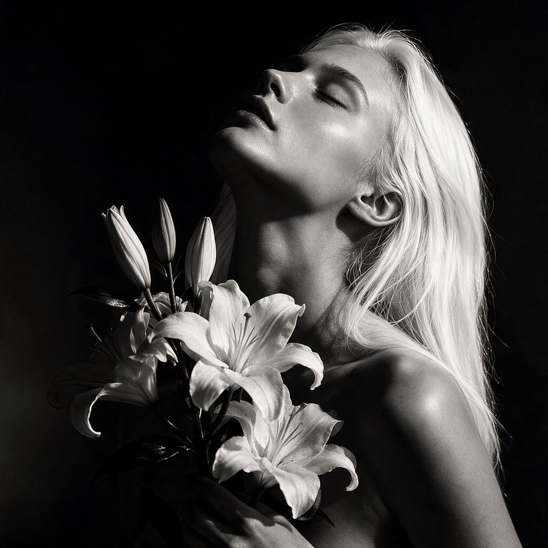 [Black and white fine art portrait of platinum blonde woman holding lily bouquet, eyes closed, tilted back against dark ba...