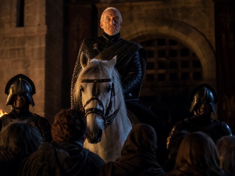 [Charles Dance as Tywin Lannister sits atop a white horse flanked by armored guards, addressing a crowd at a stone castle ...